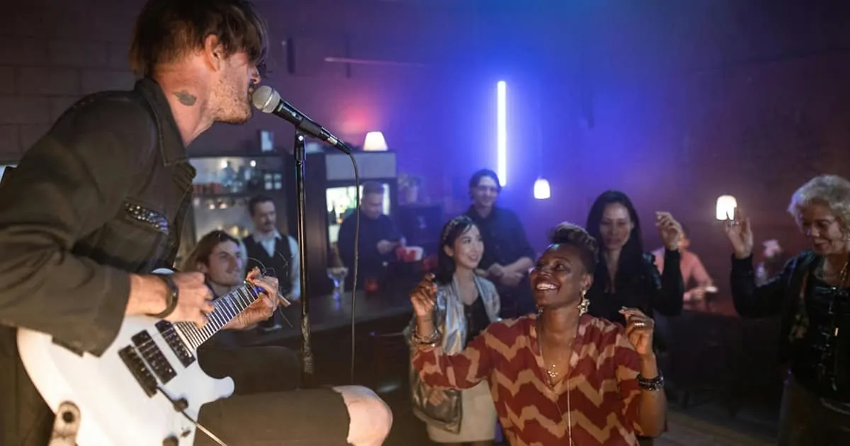 Live music performance at a vibrant nightclub with an enthusiastic audience enjoying the artist's guitar and singing, creatin