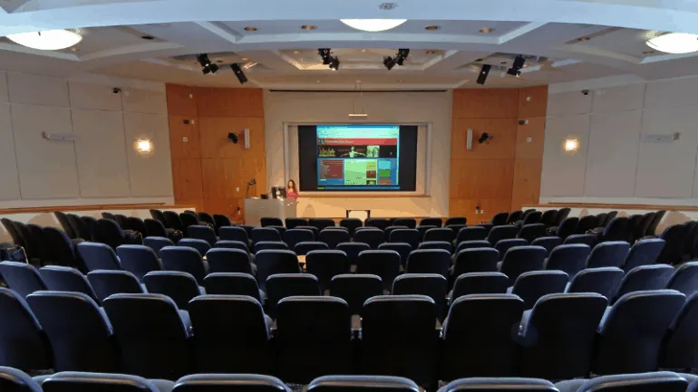 A conference room with rows of black chairs facing a large screen displaying a colorful presentation, suitable for music indu