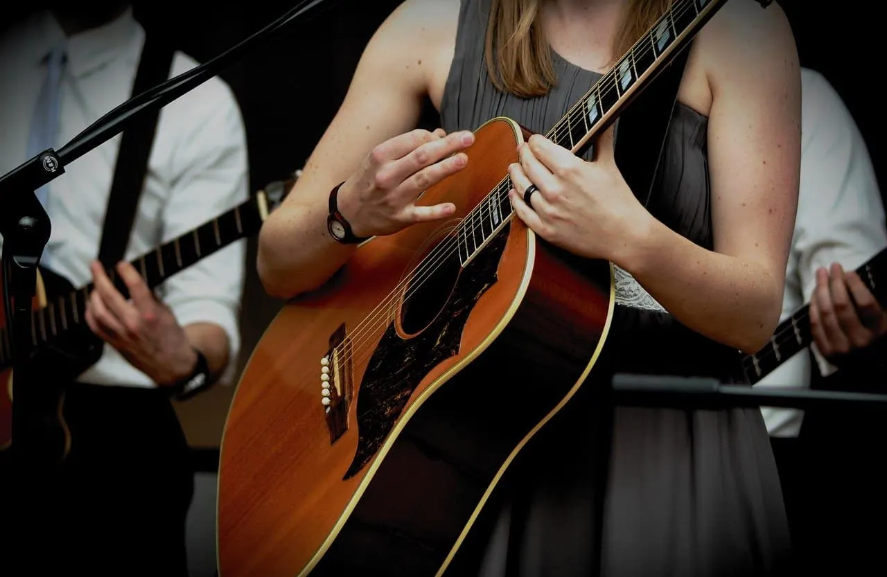 Guitarist playing acoustic guitar during live music performance, close-up of woman strumming guitar with band members in back