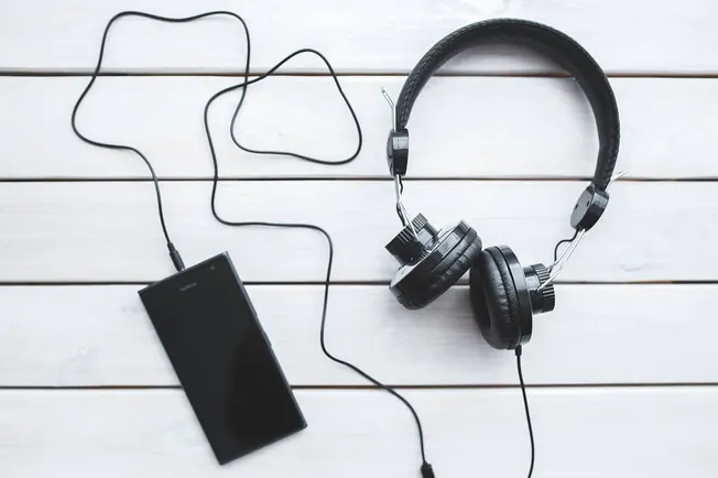 Headphones with connected smartphone on white wooden surface, music streaming technology, audio device, podcast, music listen