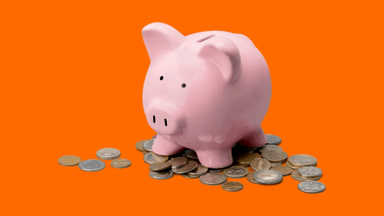 Piggy bank with coins on an orange background, representing savings, finances, and investment concepts.