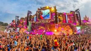 Festival crowd at electronic dance music concert with vibrant stage lighting and lively atmosphere.
